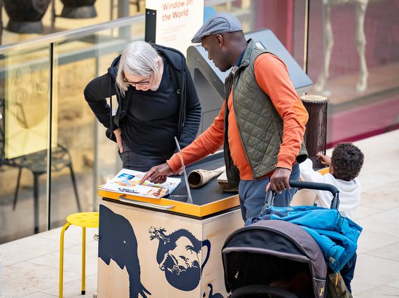 A visitor with a buggy talking to a member of staff while pointing at an open book.