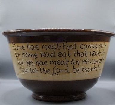 A brown and cream bowl inscribed with a Robert Burns poem in the cream part.