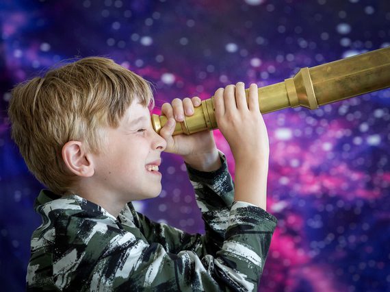Child looks towards the right through a brass telescope.