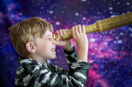 Child looks towards the right through a brass telescope.