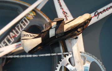 A black and white cycling shoe fixed to the pedal of a white bike.