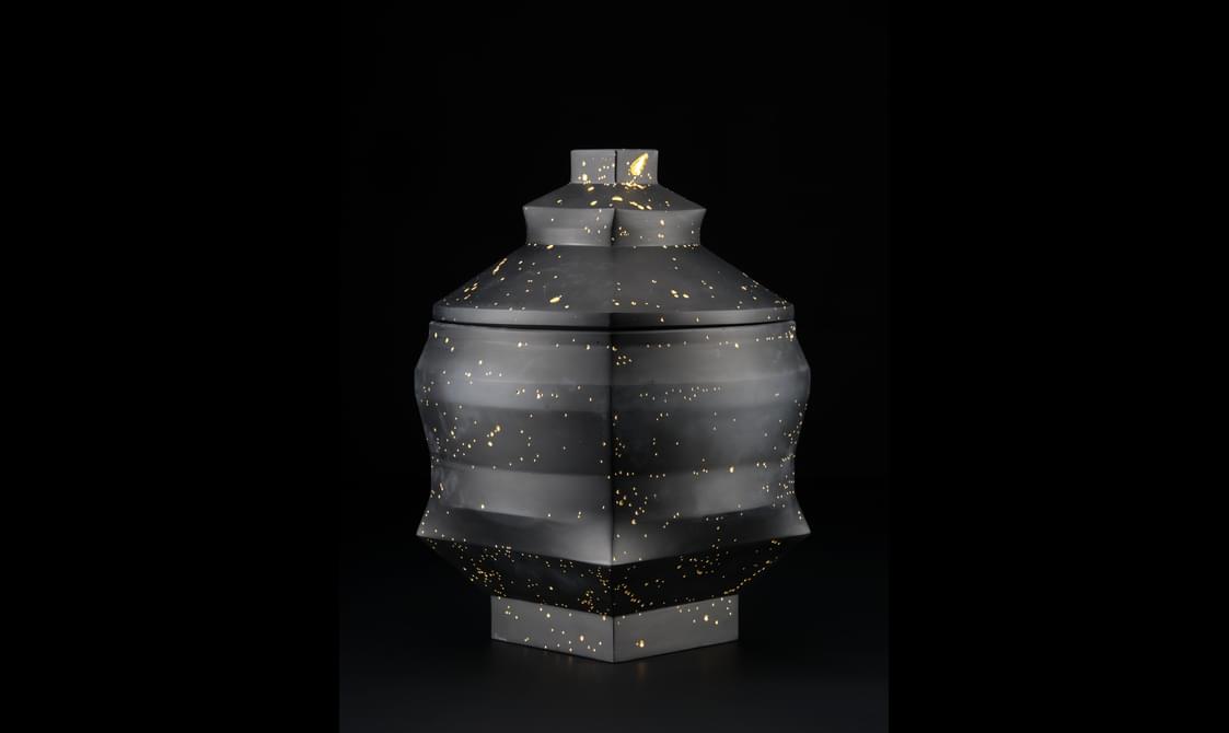 A dark coloured urn shaped sculpture piece with gold leaf inlay over tiny bubbles.