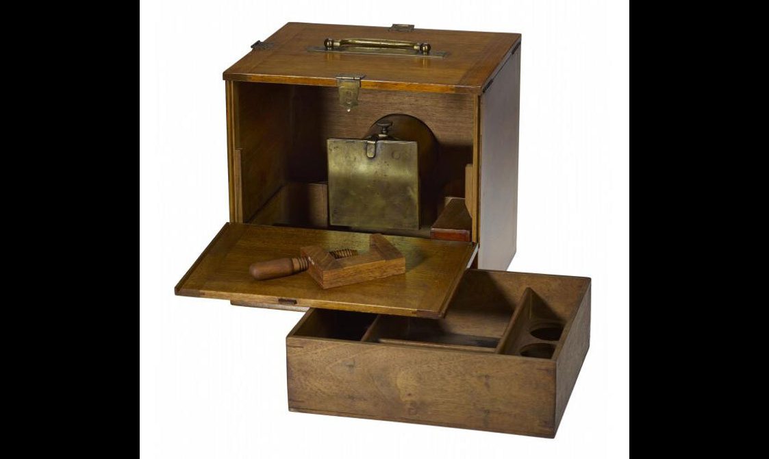 An early type of camera made of a wooden box that is open on one side to a brass square plate inside.