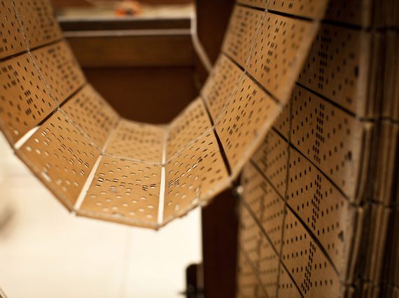 A series of light brown cards with patterns of holes punched into them sticthed together and hanging looped on a wooden frame