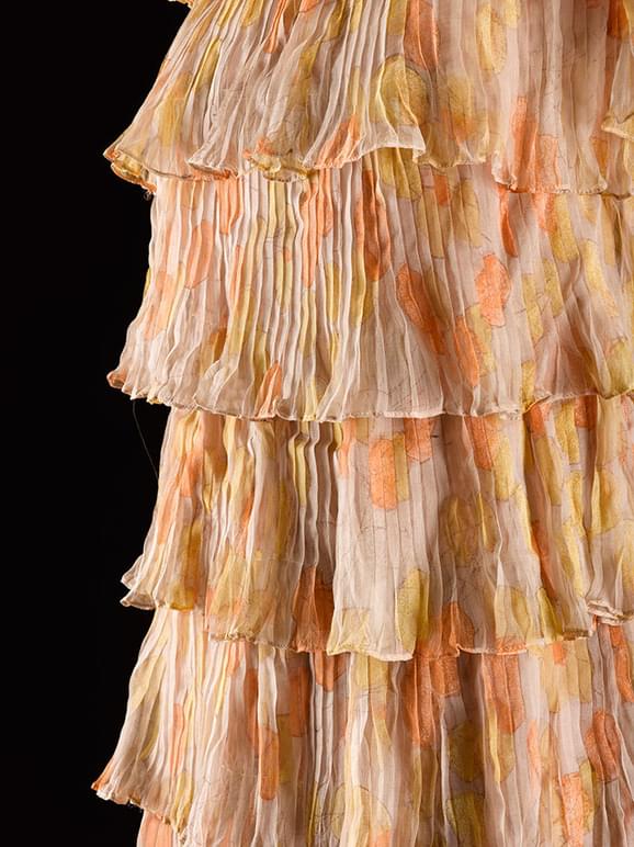 Detail of a soft orange and yellow patterend dress with silk chiffon tiers.