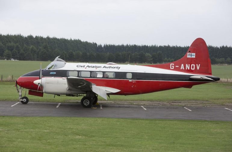 A white, red, and grey aircraft sitting on a landing strip in a grassy field.