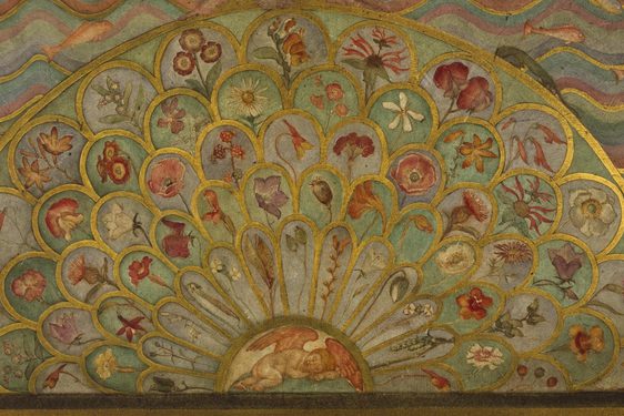 A detail of a painted wooden surface in gold, green, pink, and blue colours painted in a fanned petal like pattern