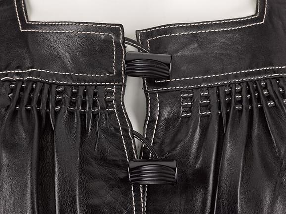 Detail of a black leather top showing white stitching and fastenings.