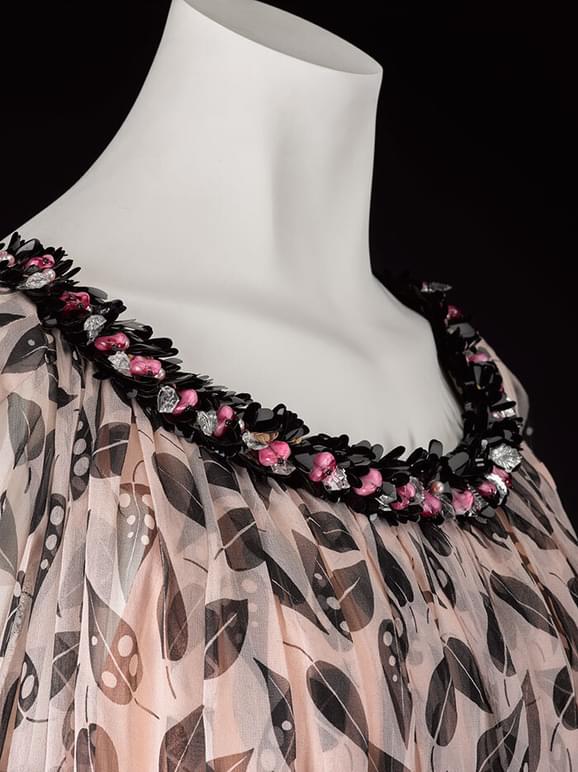 A detail of a mannequin wearing a silk georgette dress with a black and light pink pattern and a beaded neckline.