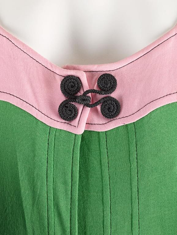 Detail of a pink and green dress with a black spiral toggle at the chest.