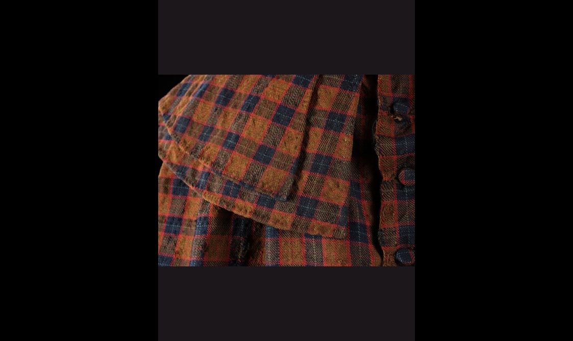 Detail of a the collar of a navy, brown, and red tartan cloak