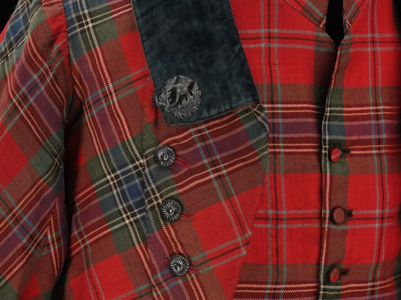 Detail of a red tartan waistcoat and jacket with decorative buttons and a navy collar.