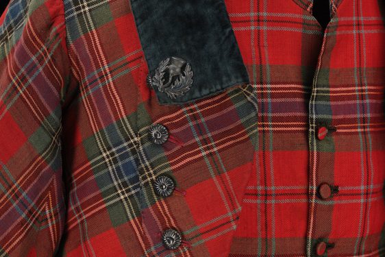 Detail of a red tartan waistcoat and jacket with decorative buttons and a navy collar.