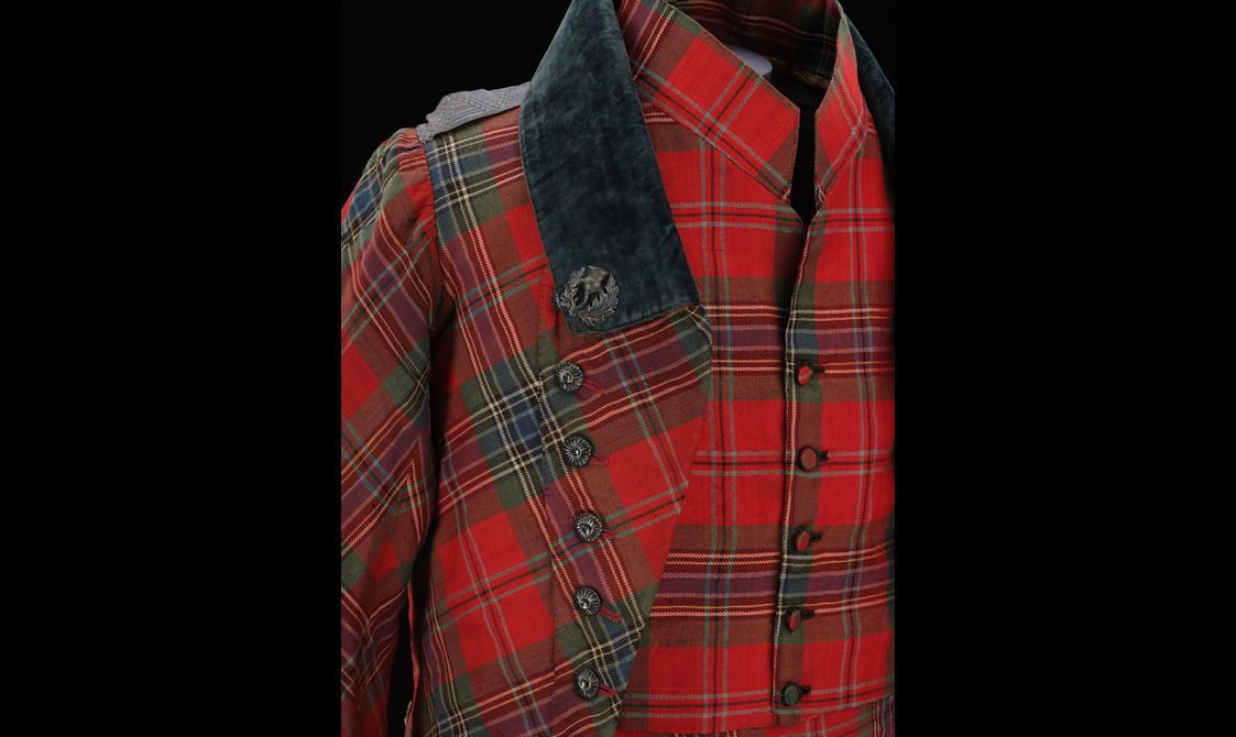 Detail of a red tartan waistcoat and jacket with decorative buttons and a navy collar.