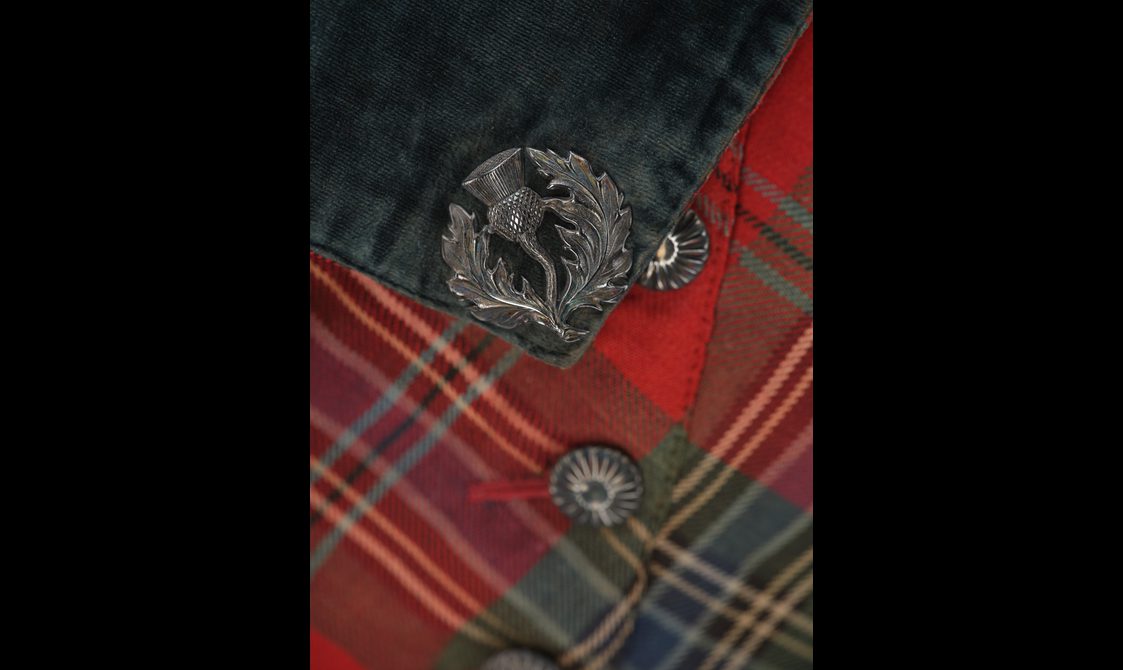 Detail of a red tartan suit showing a navy lapel with a thistle brooch.