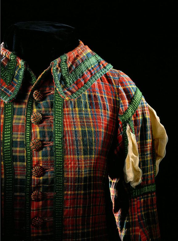 A detail of a red and green tartan jacket with buttons at the front, set against black background.