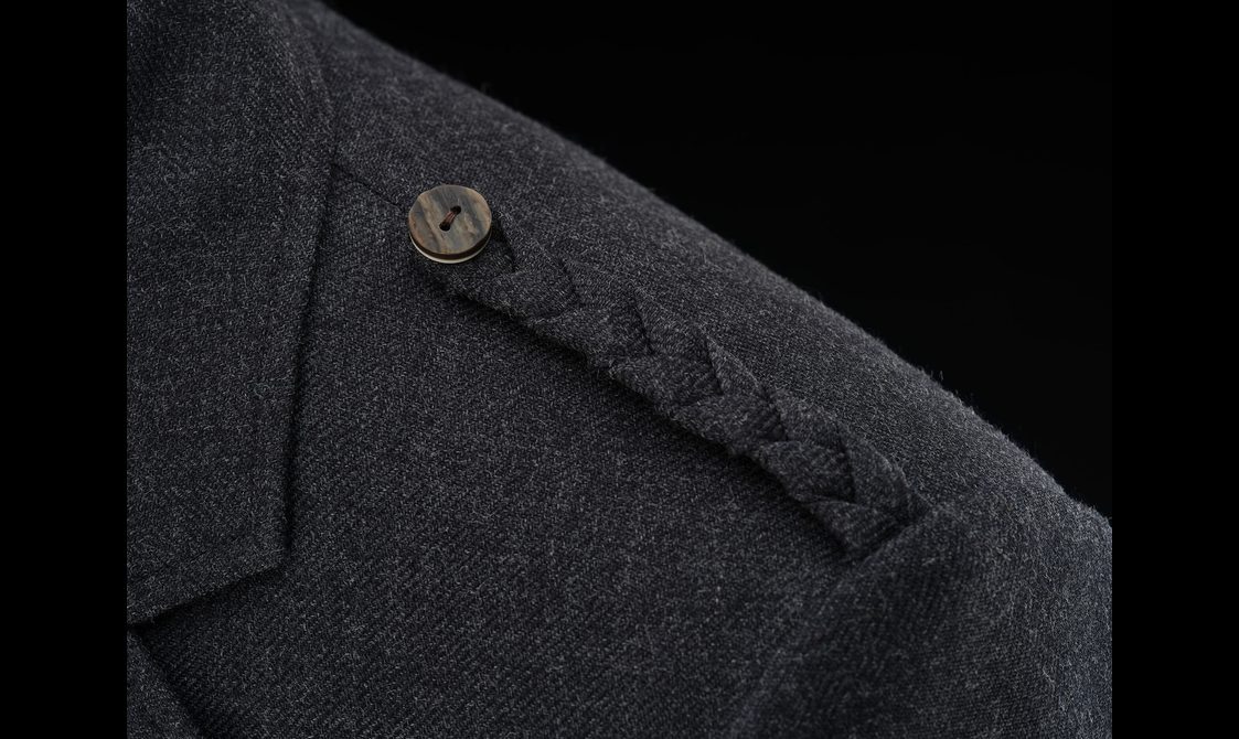 Detail of a dark grey wool jacket with a braided detail on the shoulder with a button.
