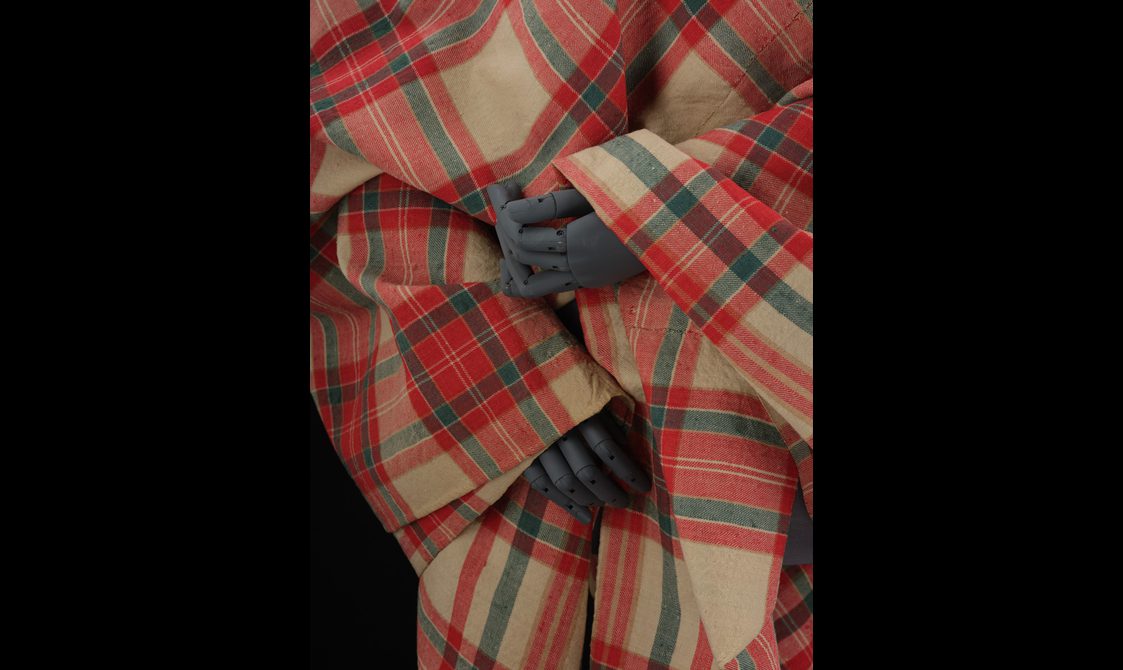Detail of a mannequin wearing a red and cream tartan shawl.