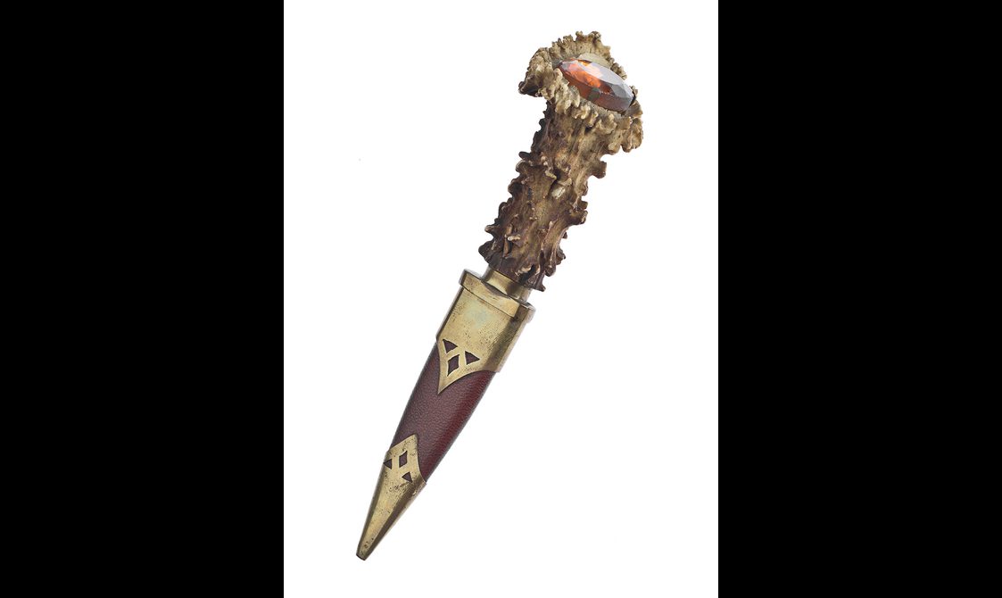 A long gold dagger. The handle is made of antler, with an orange cairngorm in the top of the hilt.