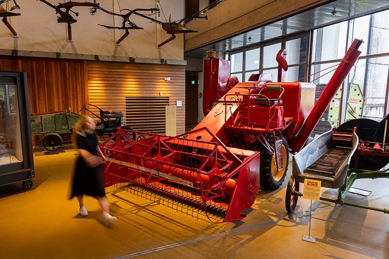 A person walking past a large red combine harvester displayed indoors at the Natural Museum of Rural life.
