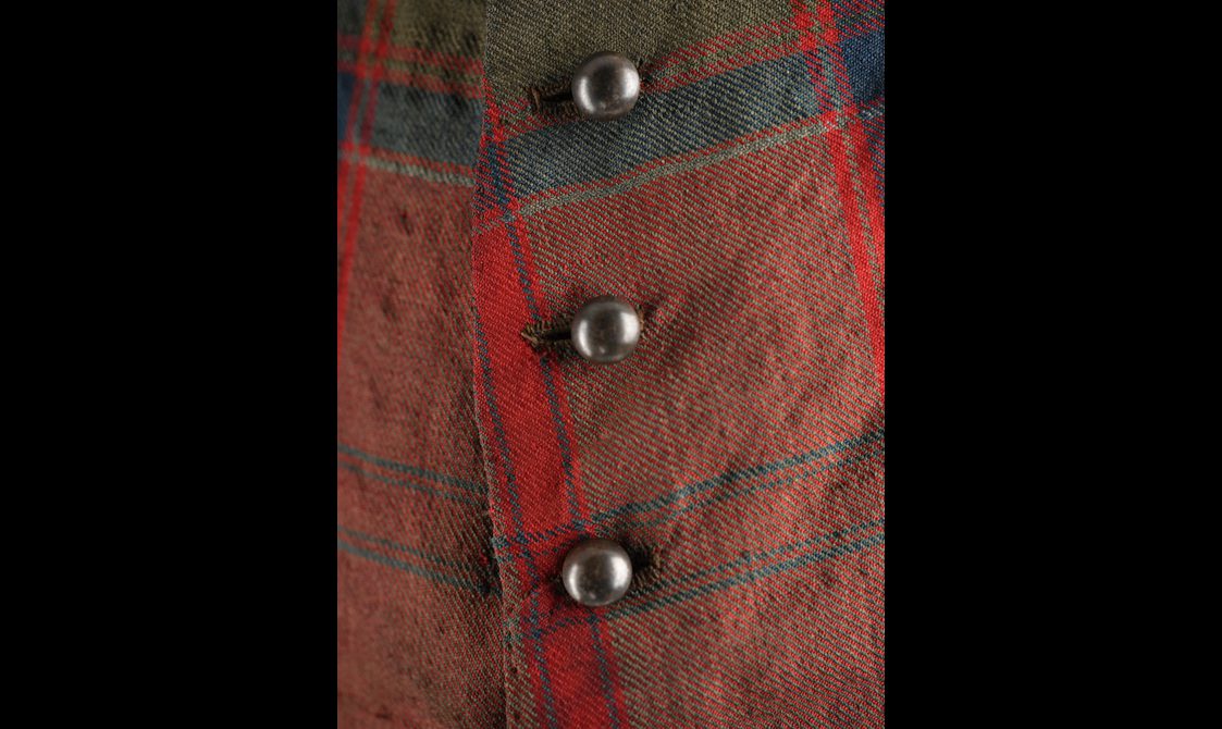 Detail of a red tartan jacket with domed metal buttons.