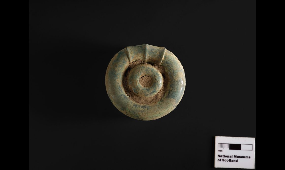 A round bronze object with a circular design in the middle