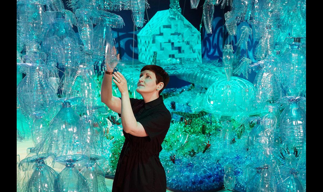 Dr Ali Clark hangs a plastic bottle in the Rising Tide exhibition, surrounded by other bottles designed to look like jellyfish.