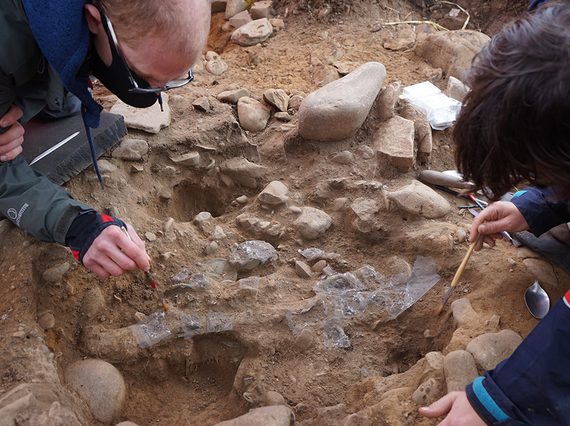 Two curators carefully brushing away surface dirt from objects in the ground