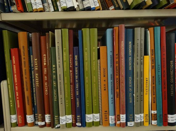 A shelf of thin, hardcover books with different coloured spines. They have library labels at the base.