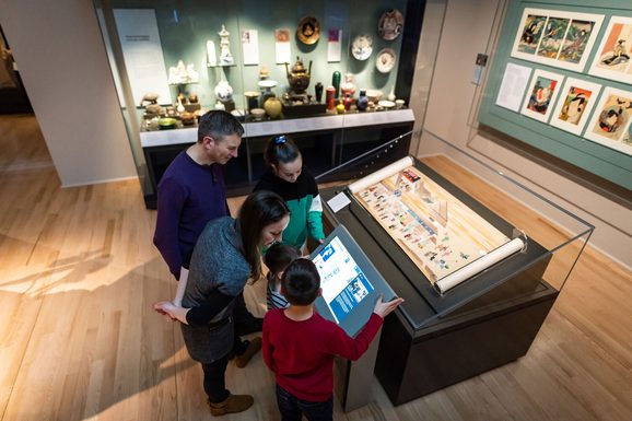 A family interacts with a touchscreen next to a display case.