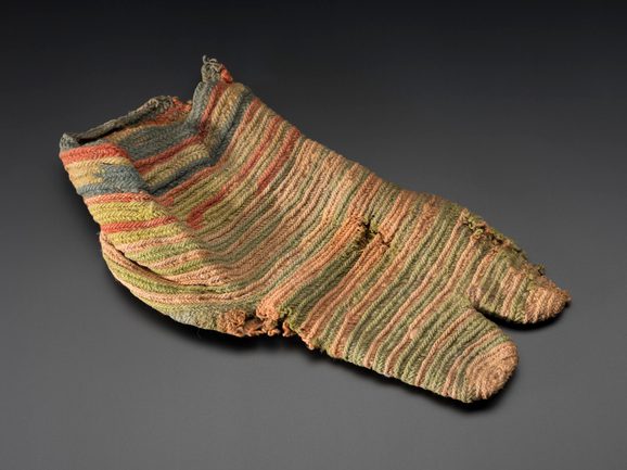 A faded striped knitted sock with a split toe design and various holes.