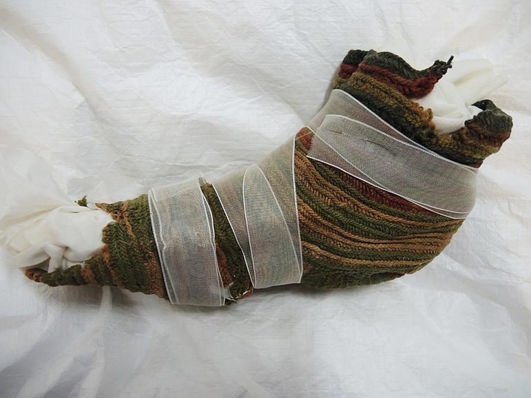 A faded striped knitted sock with various holes, wrapped in transparent white ribbon.