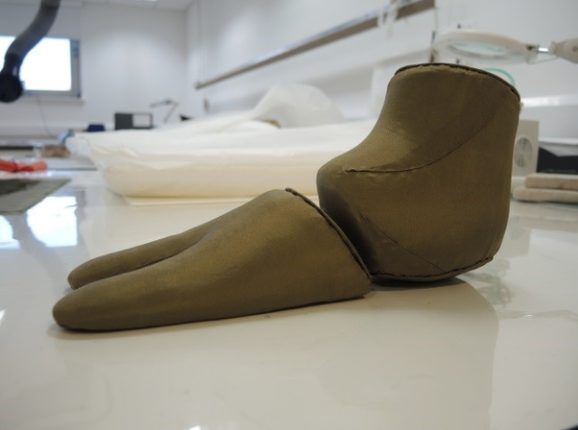 A museum display mount for a sock covered in a dark green textile.