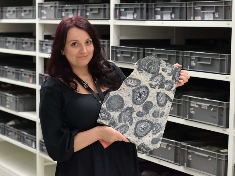 A woman wearing a black top with long dark hair holding a large piece of work with oval patterns all over its surface.