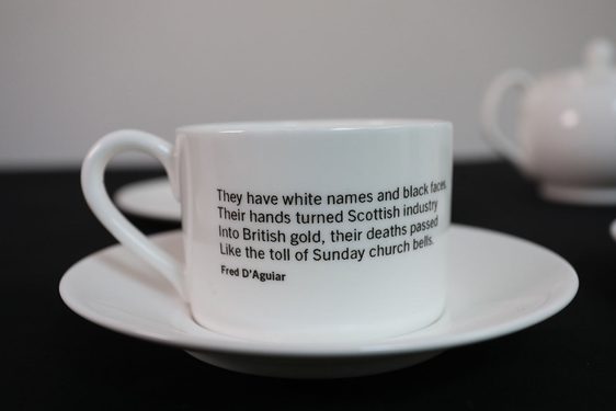 A white porcelain teacup with text written on it placed on a saucer set against blurry background.