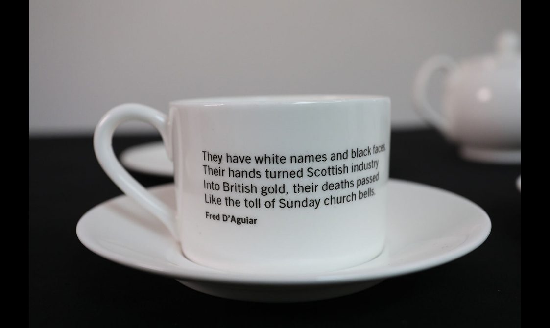 A white porcelain teacup with text written on it placed on a saucer set against blurry background.