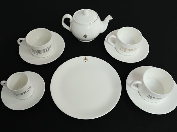 A white tea set of four cups and saucers, a teapot, and a serving plate