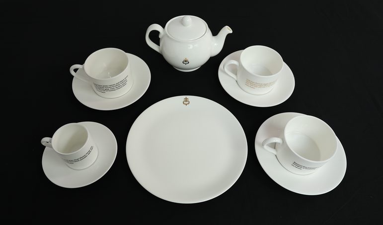 A white tea set of four cups and saucers, a teapot, and a serving plate