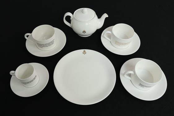 A white tea set of four cups and saucers, a teapot, and a serving plate