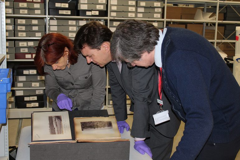 Three people standing hunched over a table looking at rare books