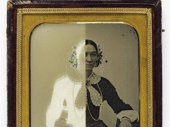 A black and white image of a woman in Victorian dress with half of the image in a white negative. The photograph has a gold border and wooden frame.