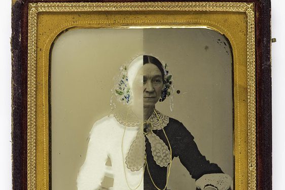 A black and white image of a woman in Victorian dress with half of the image in a white negative. The photograph has a gold border and wooden frame.