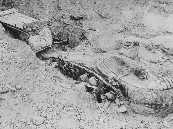 A black and white image of an ancient Egyptian coffin half buried in the soil