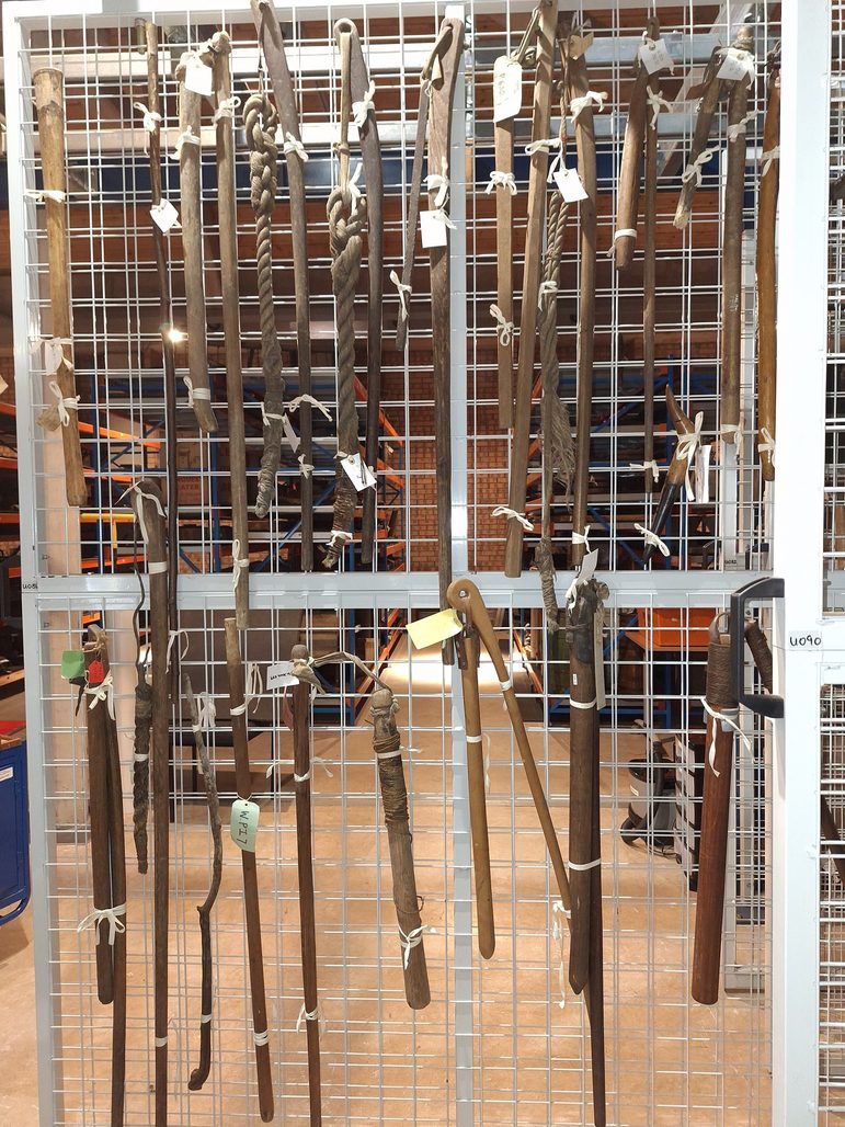 A group of flails are hung up on racking in an object store.