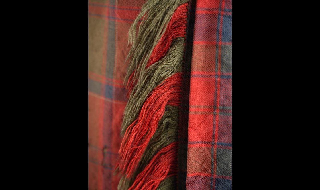 Detail of a red tartan textile with a fringed edge.
