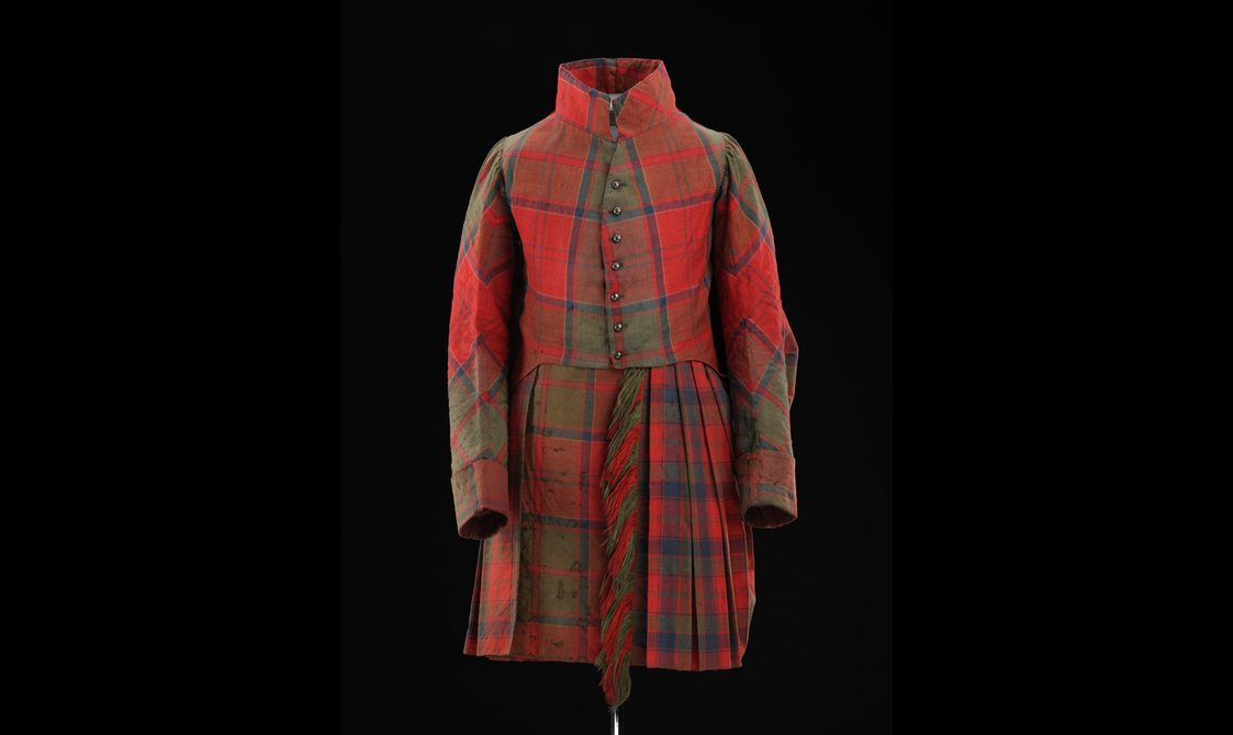 A mannequin wearing a red tartan kilt with a matching high collared jacket.