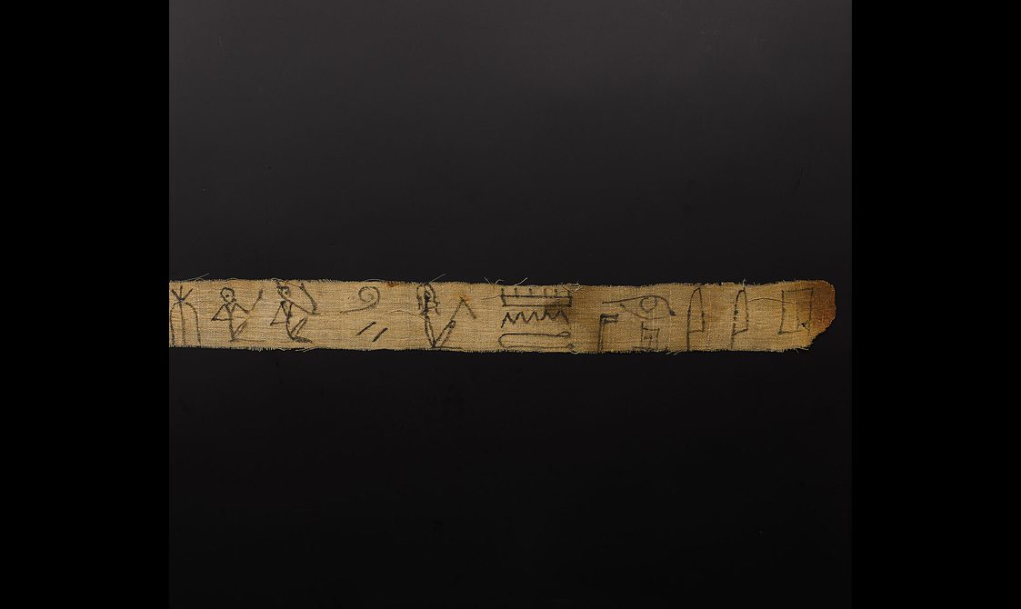 A fragment of an old Egyptian bandage with hieroglphs drawn in black ink.