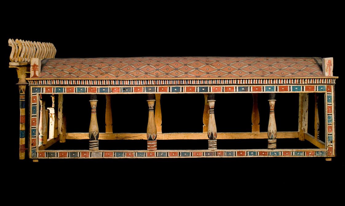 A wooden structure of pillars and a roof with decorative painted surfaces.