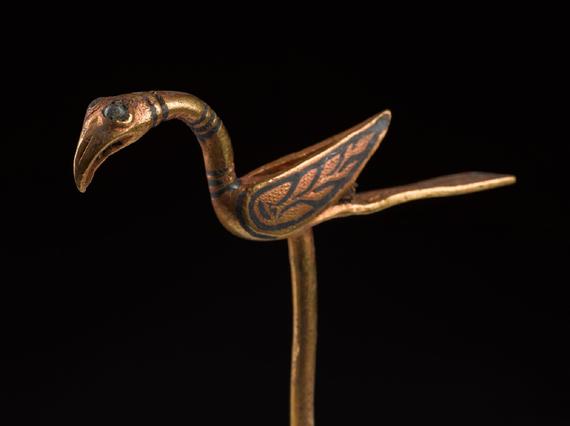 Golden pin shaped like a bird, with long, flat tail, upturned wings and flamingo-like beak.
