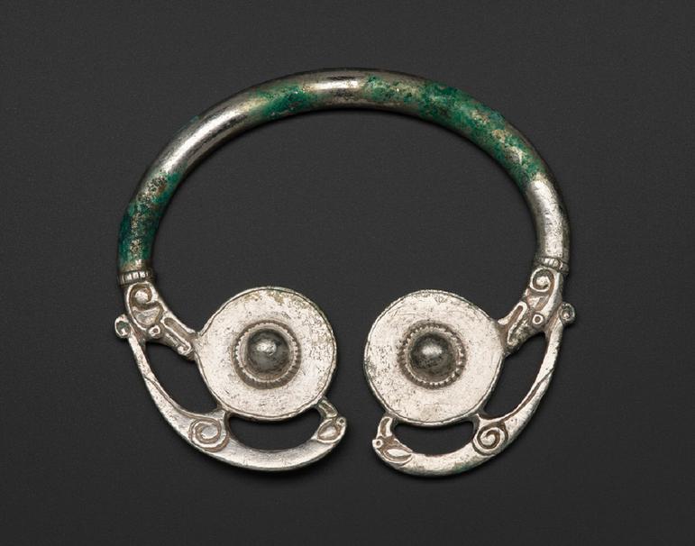 A brooch featuring two silver disks joined by a looped silver rod